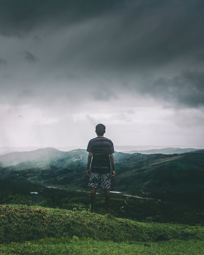 男人站在草地上面临的山脉在白天
